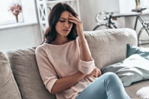 Frustrated young woman suffering from the headache while sitting on the sofa at home. How to Handle Stressful Situations Instead of Living in Hope Of a Cure