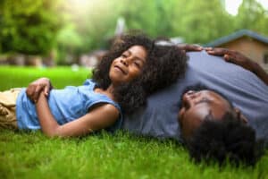 African-American son and father rests on grass at backyard holiday villa. Maintain an Optimistic Outlook For a Happy Life