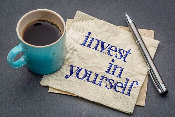 Invest in yourself advice or reminder - handwriting on a napkin with cup of coffee against gray slate stone background. Free tips and advice for self-improvement