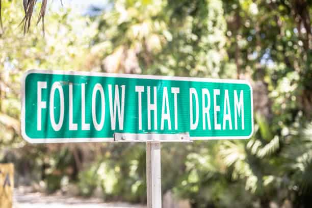 Motivational quote saying Follow That Dream on a sign next to a road in the nature. Do what you love
