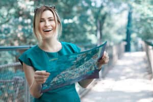 lifestyle shot of blond hair woman holding map and smiling, enjoying her city break in summer day. Happiness's Road Map