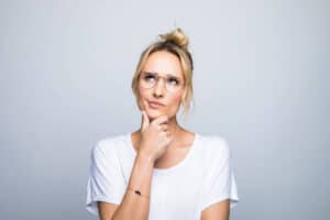 Thoughtful blond woman with hand on chin looking up against gray background. Utilize Your Thoughts' Power