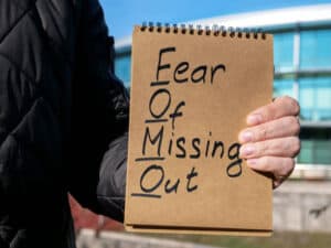 Man holds page with words FOMO fear of missing out. What are you missing out on