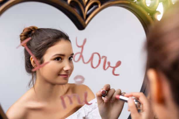 Portrait of a beautiful caucasian girl looking in the mirror and writing I love me near a heart, self-love. High quality photo. You Make Me Feel