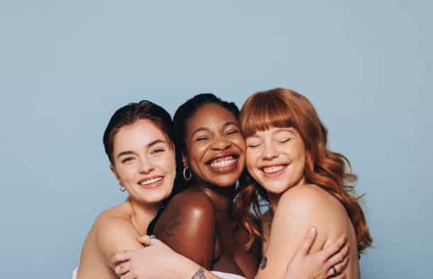 **Diverse women, radiating happiness, embracing in a studio. Celebrating authentic selves and the essential role of friendship.**