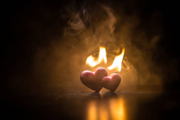 Valentine's backdrop: Heart on a dark wooden table amidst burning hearts in fiery surroundings. Symbolizing Passion Fire In Your Soul.