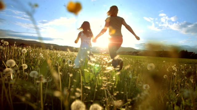 In super slow motion, a mother and her little daughter run through a meadow at sunset, creating a joyful moment.