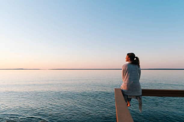 Young woman sitting on edge looks out at view sunset and sea behind, Michigan healthy boundaries stock pictures, royalty-free photos & images